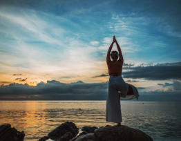 Frau in einer Yoga-Stellung auf einem Stein und mit Blick auf das Meer