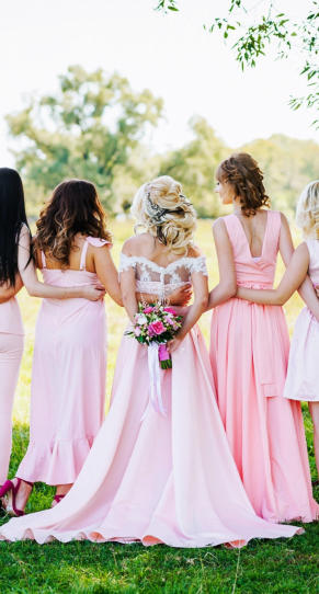 Braut mit Junggesellenen in pinken Kleidern auf einer Wiese 