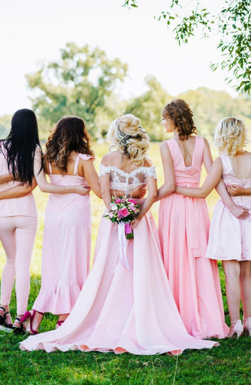 Braut mit Junggesellenen in pinken Kleidern auf einer Wiese 